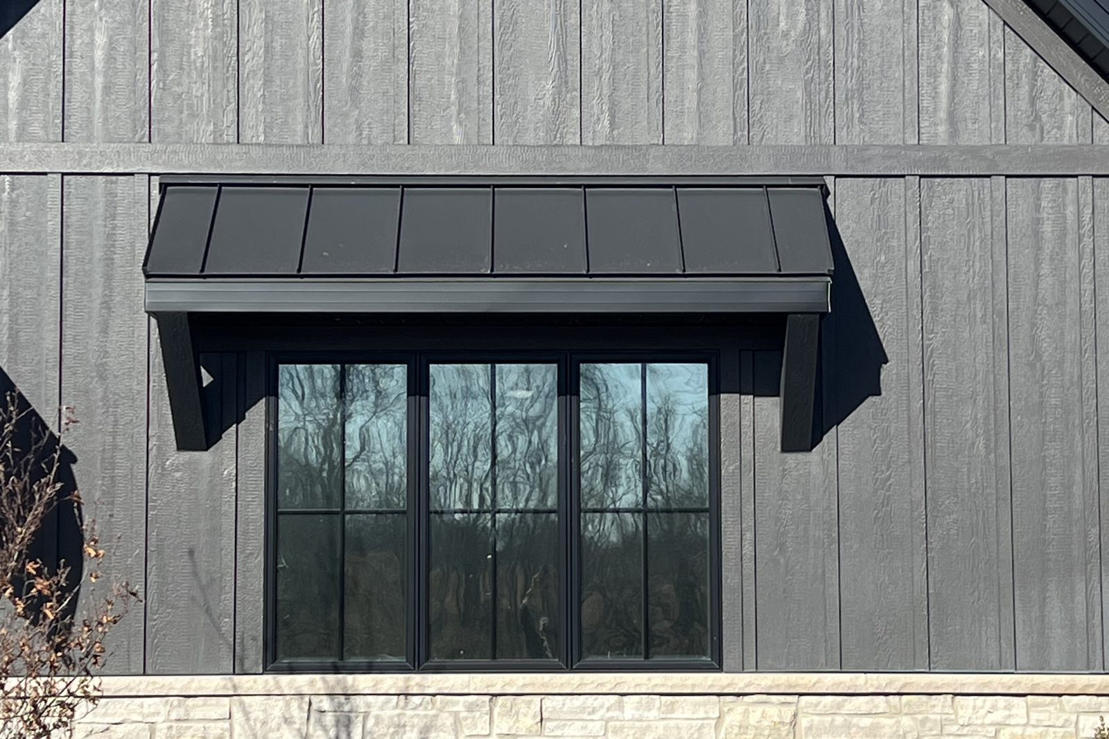 Grey board-and-batten home with black-frame windows fitted with window film