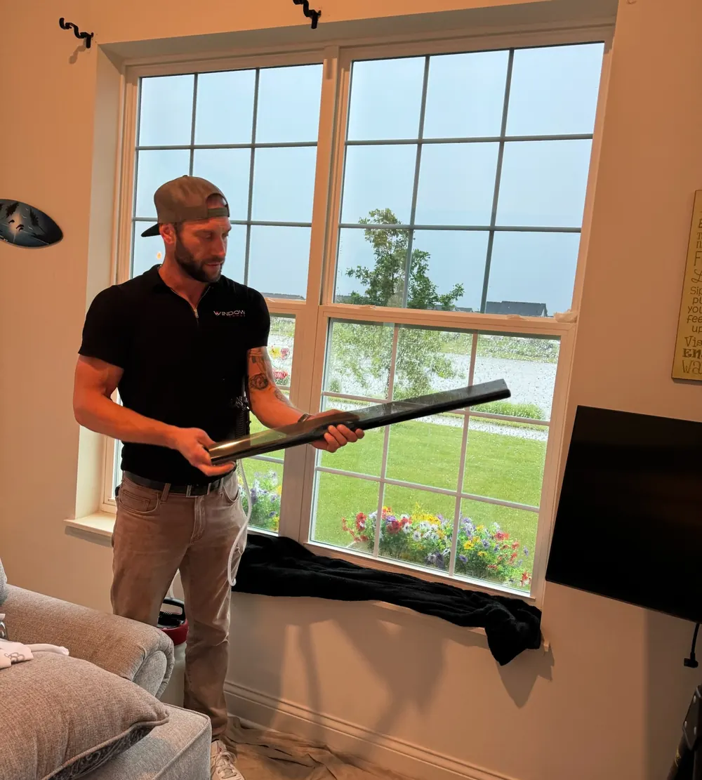 Installer holding a roll of window film beside living room windows during a residential window tinting job in Cedar Lake, IN